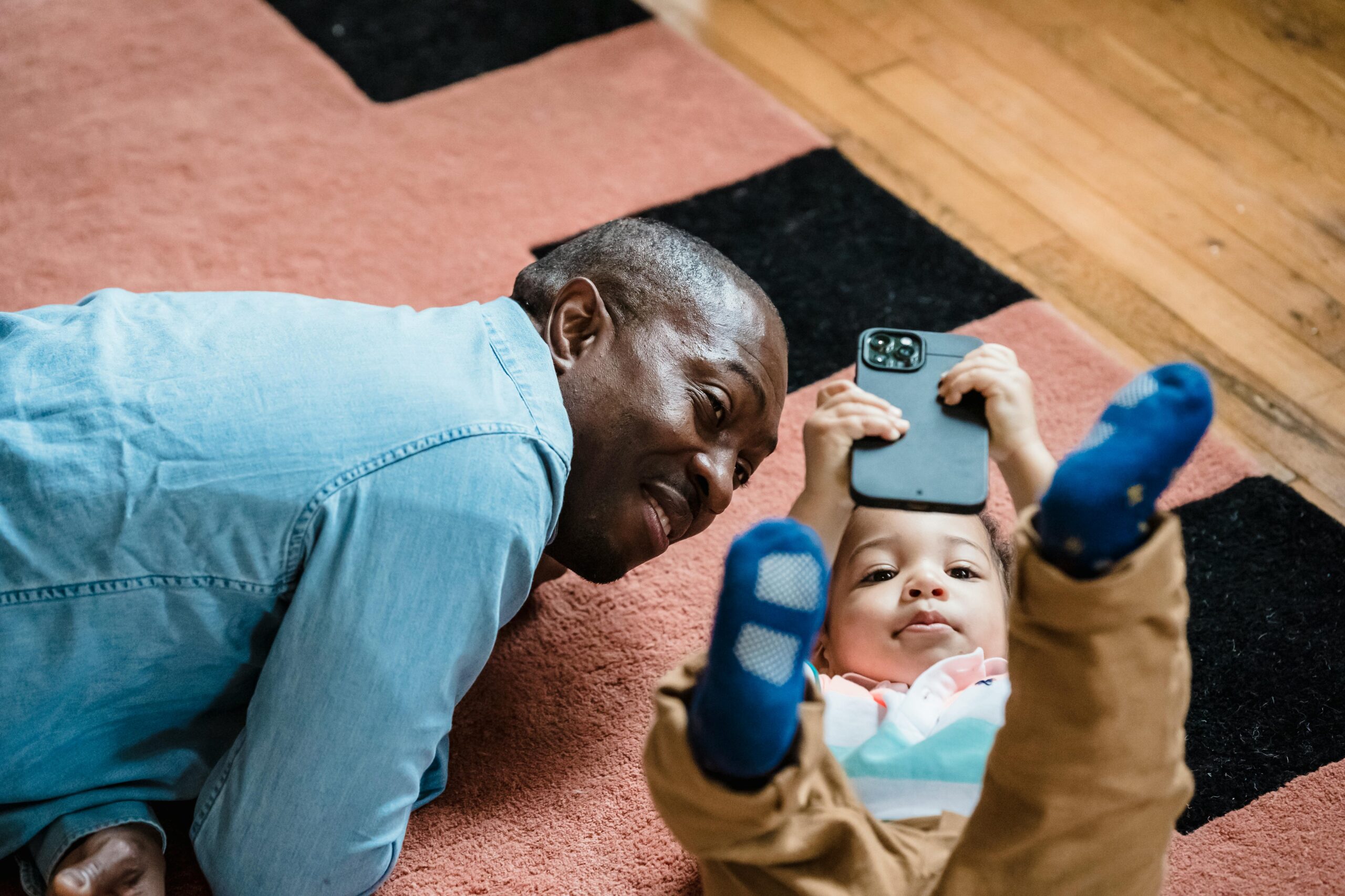 A child plays on a smartphone with their father next to them.