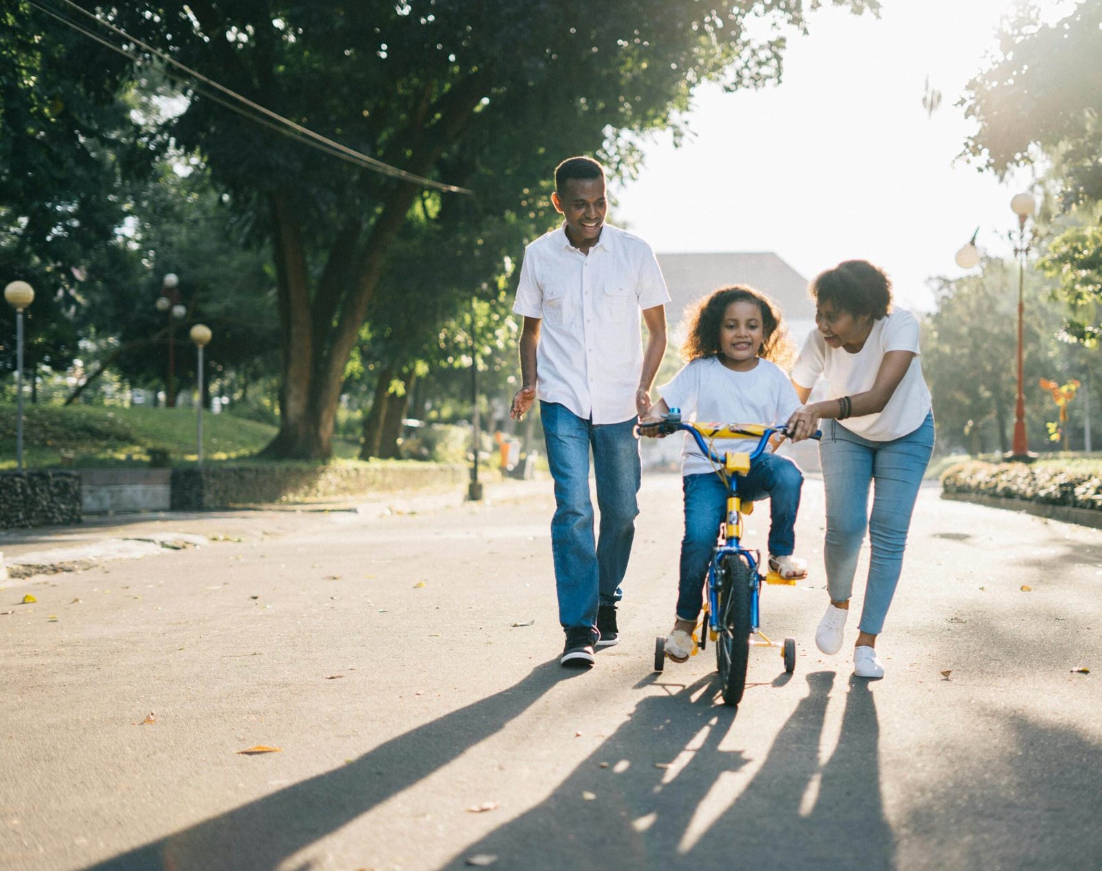Two parents are teaching their child how to ride a bike outside.